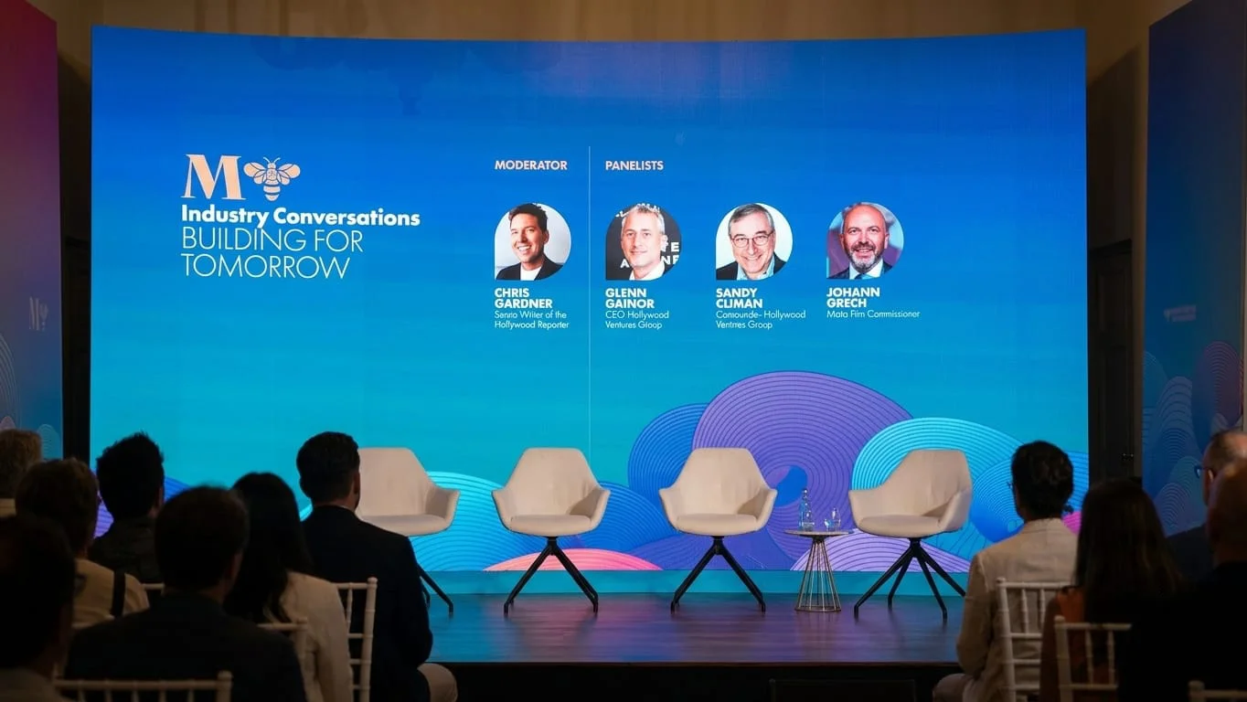A panel stage at the Mediterrane Film Festival in Valletta. A large screen reads 'Industry Conversations: Building for Tomorrow' above four empty chairs, with a seated audience in the foreground.